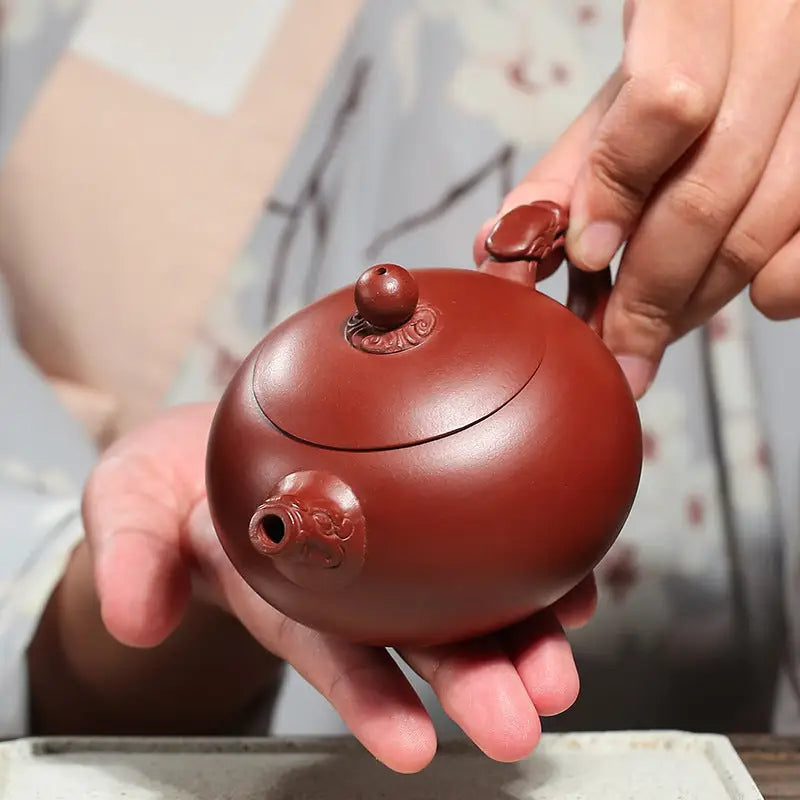 Round reddish-brown Silent Sentinel yixing zisha teapot with ornate details featuring authentic purple finish