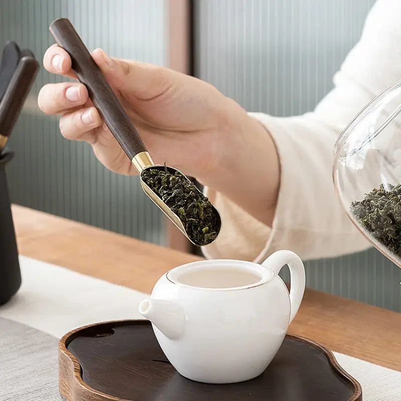 Tea scoop pouring tea leaves into a white teapot in the Six Gentlemen Tea Set for Gongfu Tea Ceremony