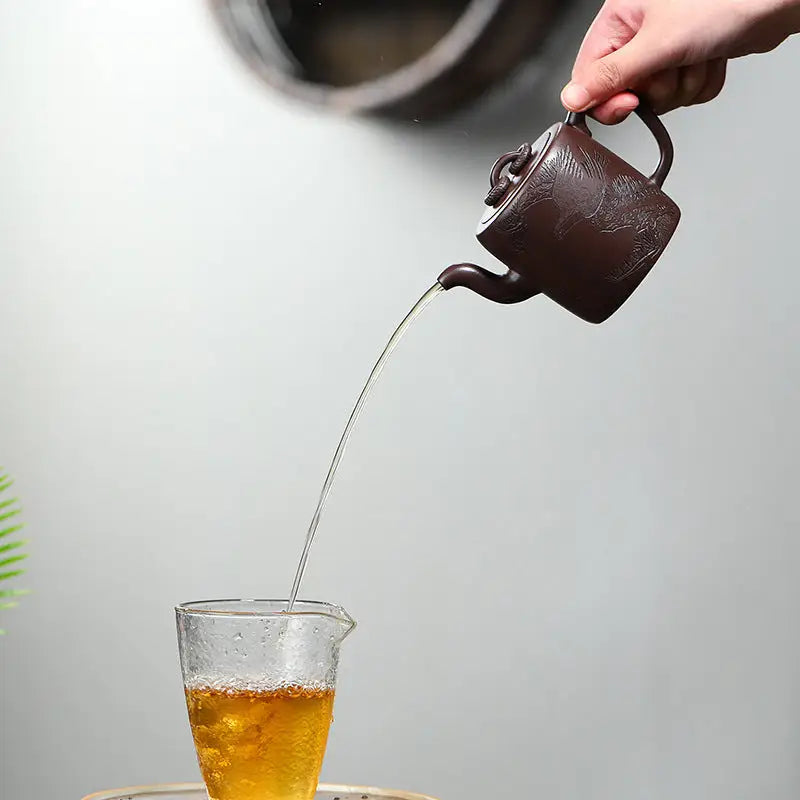 Brown Yixing Zisha Teapot Soaring Tranquility pouring liquid with carved crane and pine motif