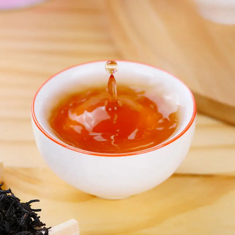 White teacup with splashing amber liquid showcasing Sou Chong Red Tea Leaves and tea sets