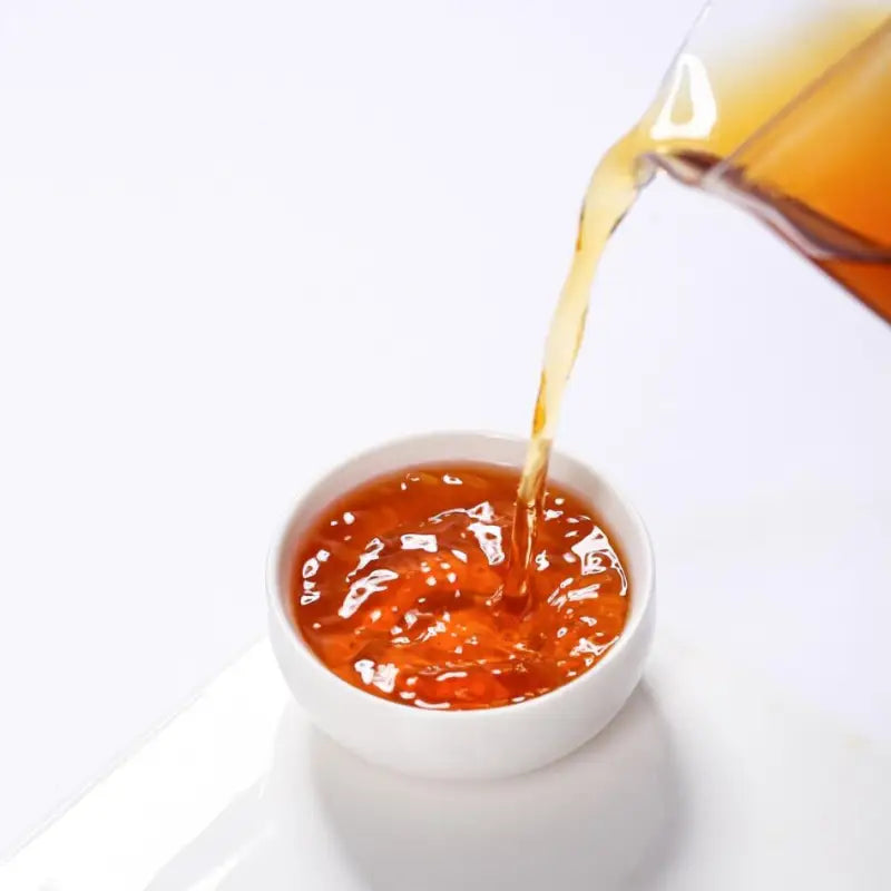 Orange liquid pouring into a white bowl showcasing Spring Beauty Tanyang Gongfu Black Tea craftsmanship