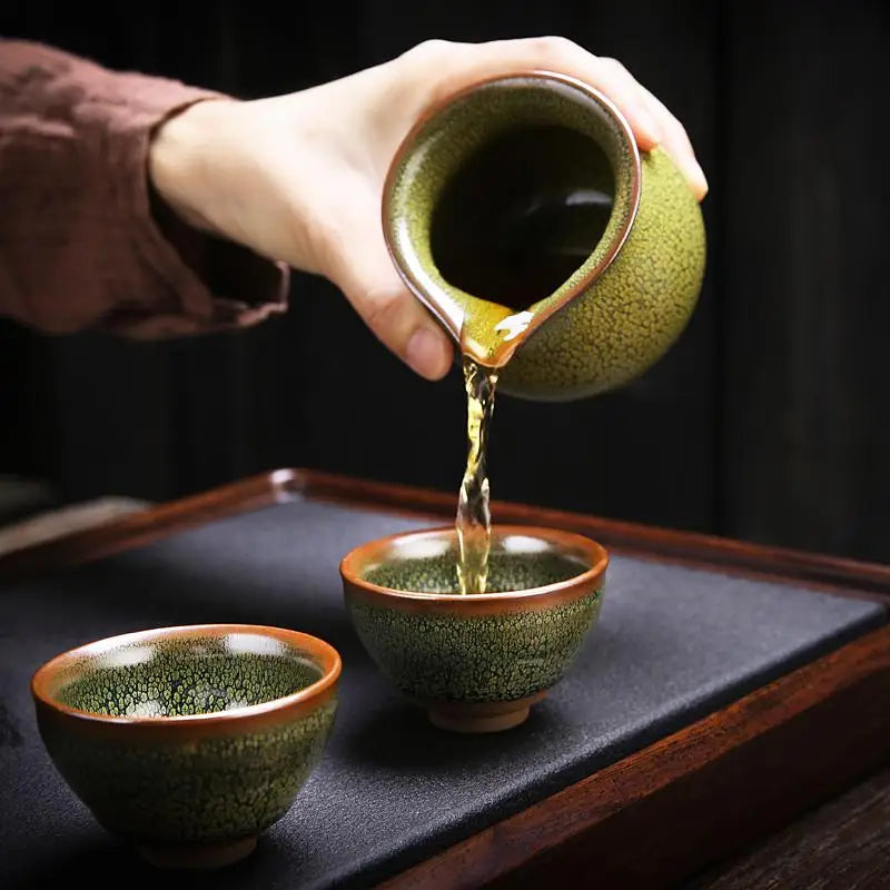 Green tea being poured into a matching cup from the Sunflower Tea Set made with Jianyang glaze for gongfu tea