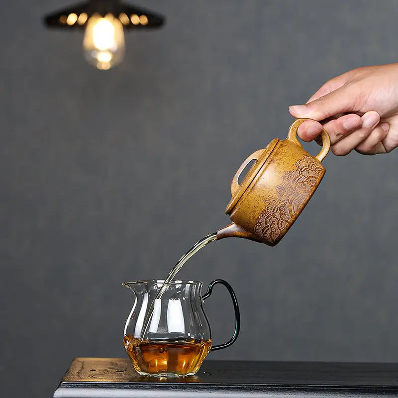 Tea being poured from a patterned Temple Ridge Yixing Duanni teapot into a glass pitcher