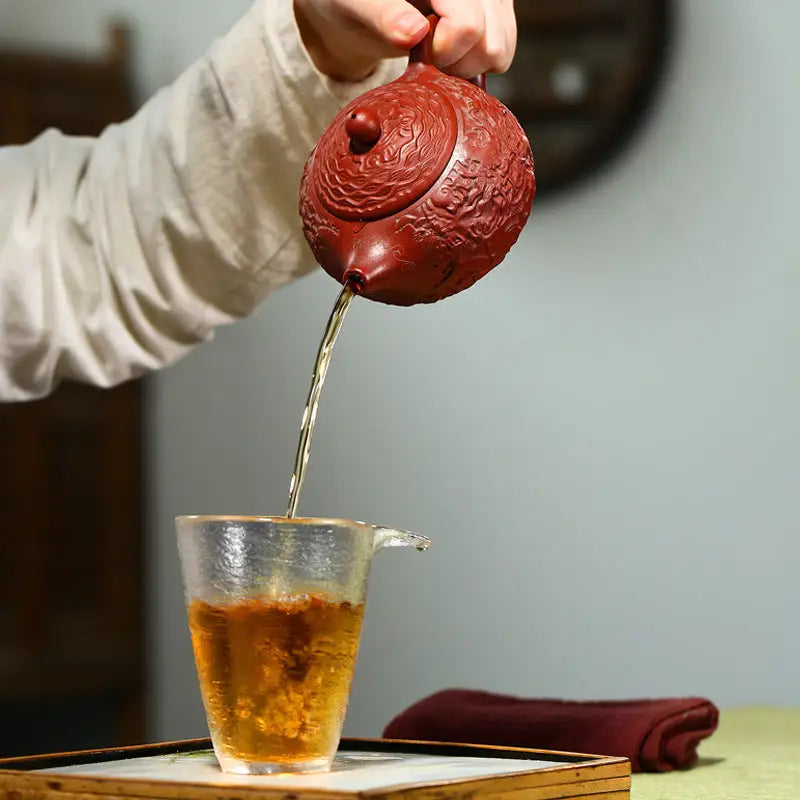Red clay teapot pouring tea showcasing yixing zisha clay with dragon relief design