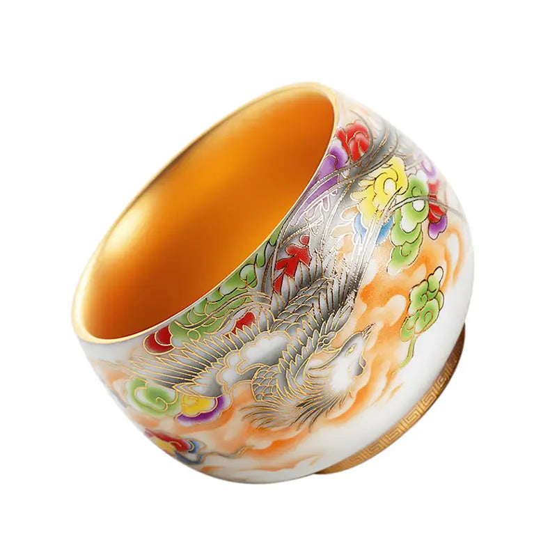 Ornate gold-lined porcelain tea cup with colorful floral and bird designs from The Phoenix