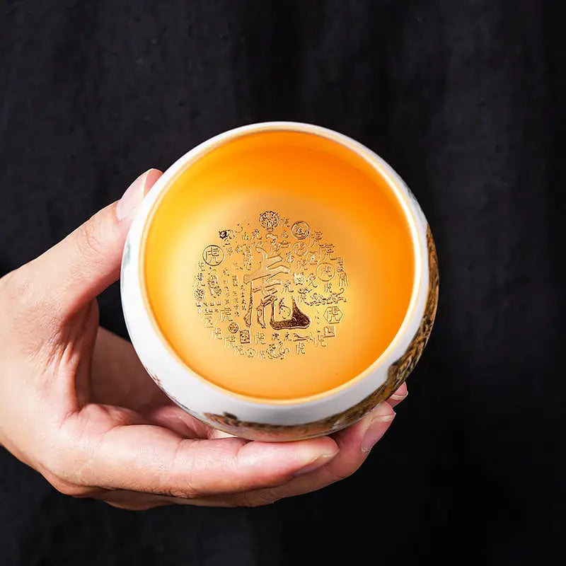 Hand holding a golden-lined ceramic bowl from The Tiger tea set for gongfu tea brewing