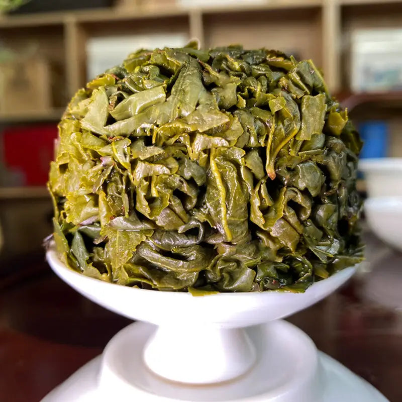 Pile of green tea leaves for Tie Guan Yin High Mountain Tea in teapots and tea sets
