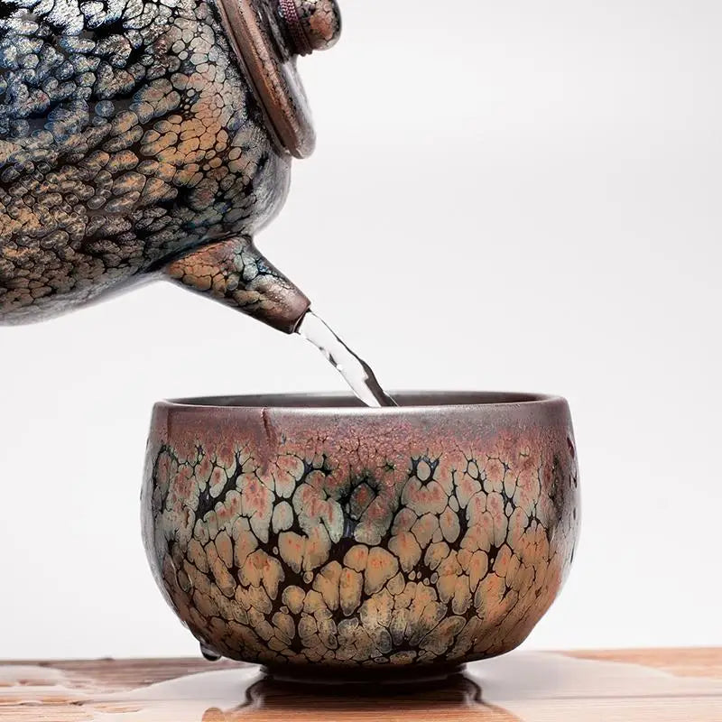 Glazed ceramic teapot pouring into cup showcasing handcrafted Jianyang crystalline glaze