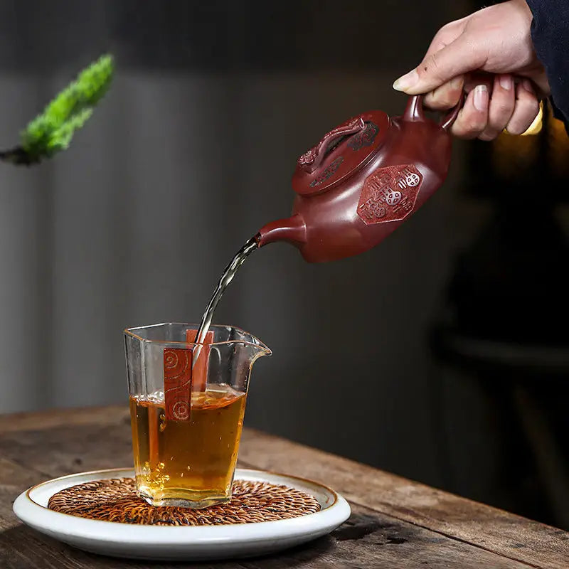 Tea being poured from a Treasure Blessing yixing zisha teapot into a glass with five gourds