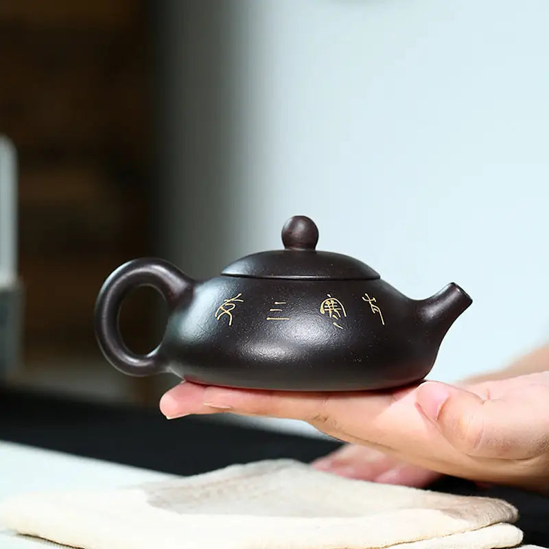 Dark brown ceramic teapot from Twilight Plum Yixing with hand-painted plum blossoms in black zisha clay