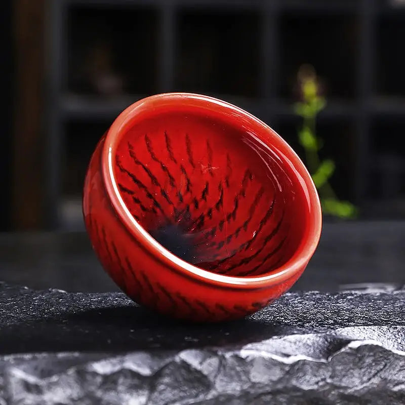 Red ceramic tea cup with dark swirling pattern showcasing Jian Zhan blood-red glaze teacup and bold crimson Zhan design