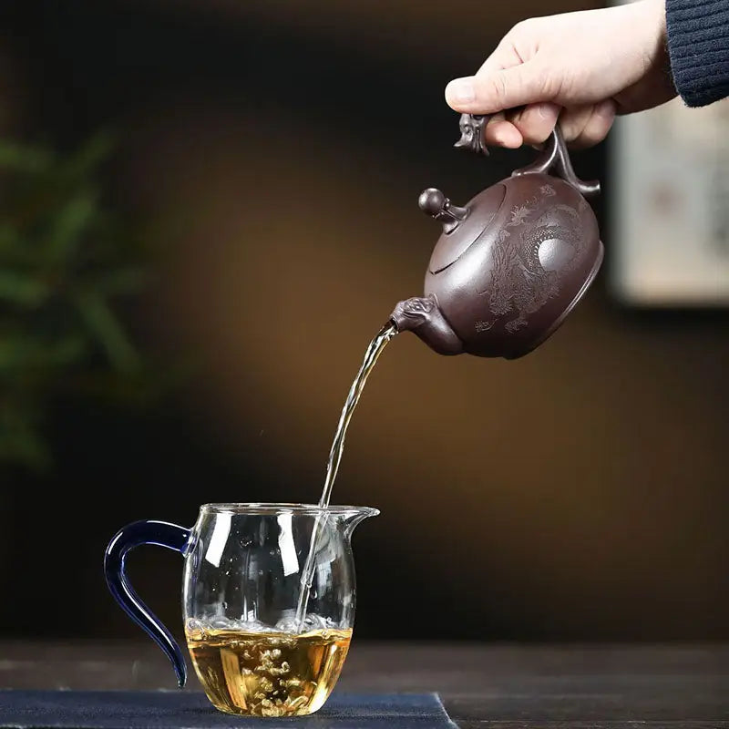 Tea being poured from a wandering dragon Yixing dragon Zisha teapot into a glass pitcher