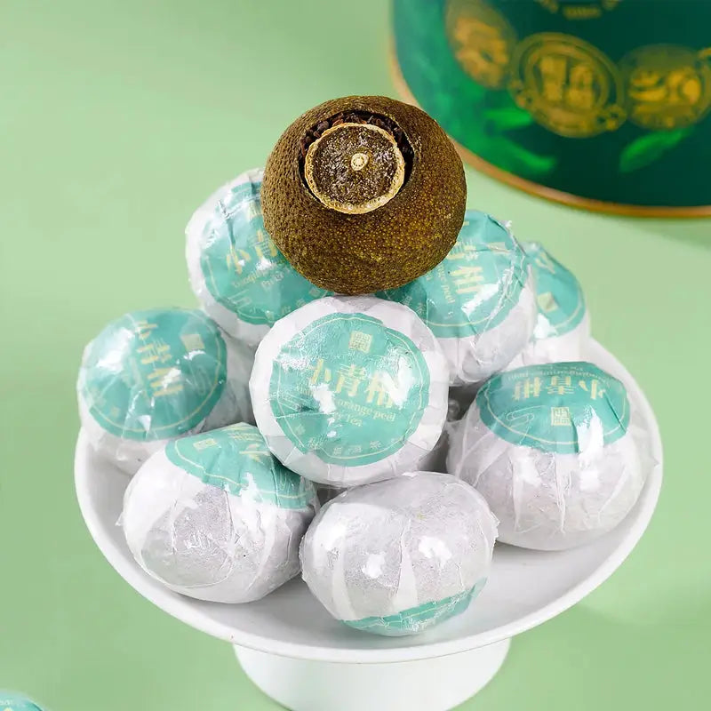 Pile of wrapped Xiao Qing Gan Pu’er Tea Leaves with citrus fruit, perfect for tea sets