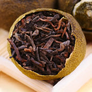 Tea-filled citrus fruit showcasing Xiao Qing Gan Pu’er Tea Leaves with teapots and mugs