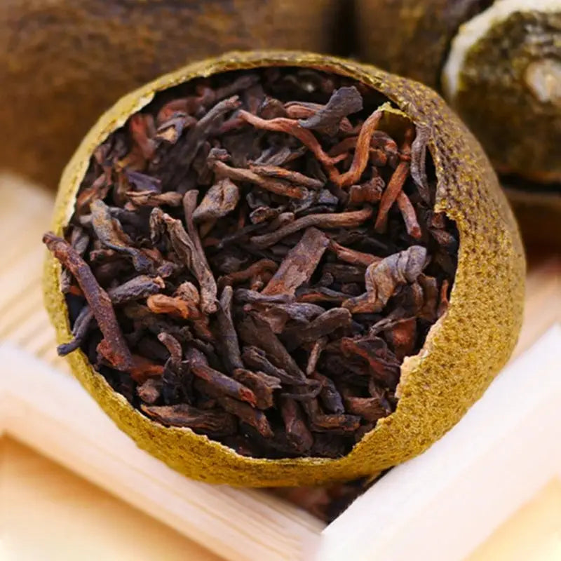 Tea-filled citrus fruit showcasing Xiao Qing Gan Pu’er Tea Leaves with teapots and mugs